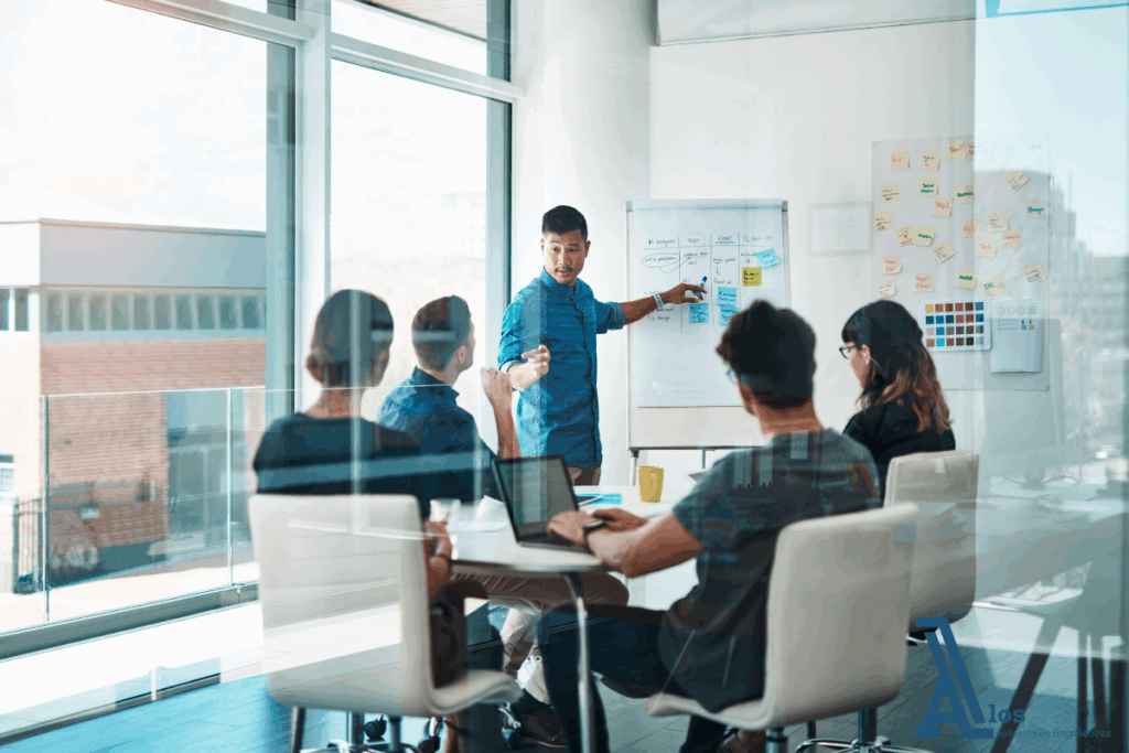 Imagen de una sesión de formación en idiomas en una sala de reuniones, con un docente explicando vocabulario o frases clave mientras varios profesionales toman apuntes. Refleja el compromiso empresarial con el desarrollo de competencias lingüísticas internas.