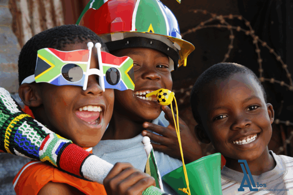 Tres niños sosteniendo banderas de Sudáfrica, con el niño del centro usando un silbato de fútbol y sonriendo al frente