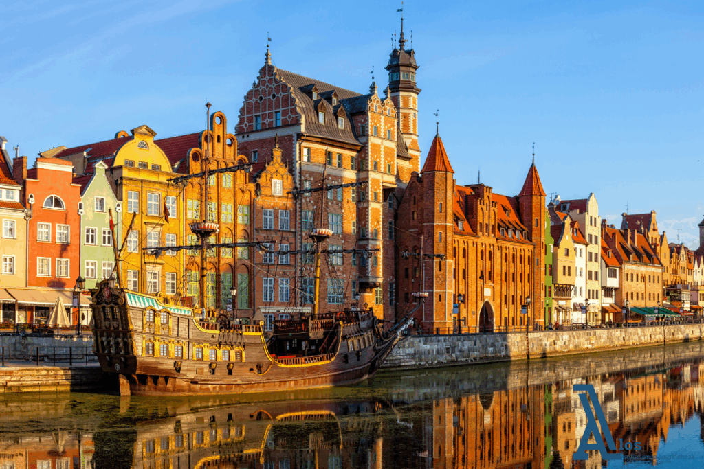 Vista panorámica del puerto histórico de Gdańsk con un barco turístico navegando frente a casas de arquitectura hanseática.


