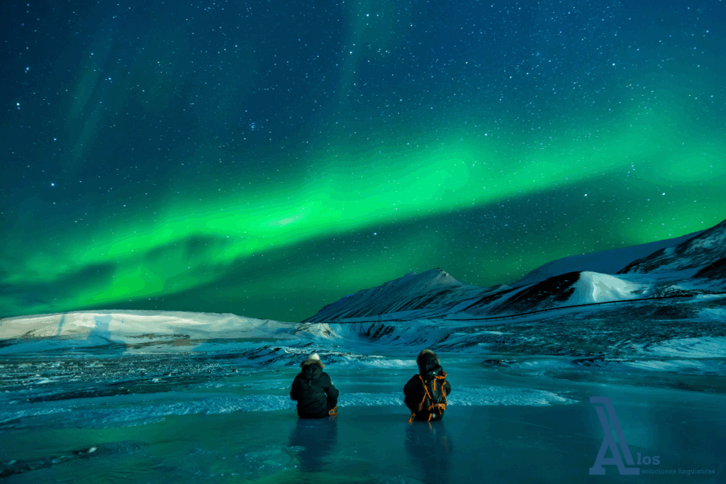Dos personas observando auroras boreales sobre montañas pequeñas con nieve al fondo durante la noche.