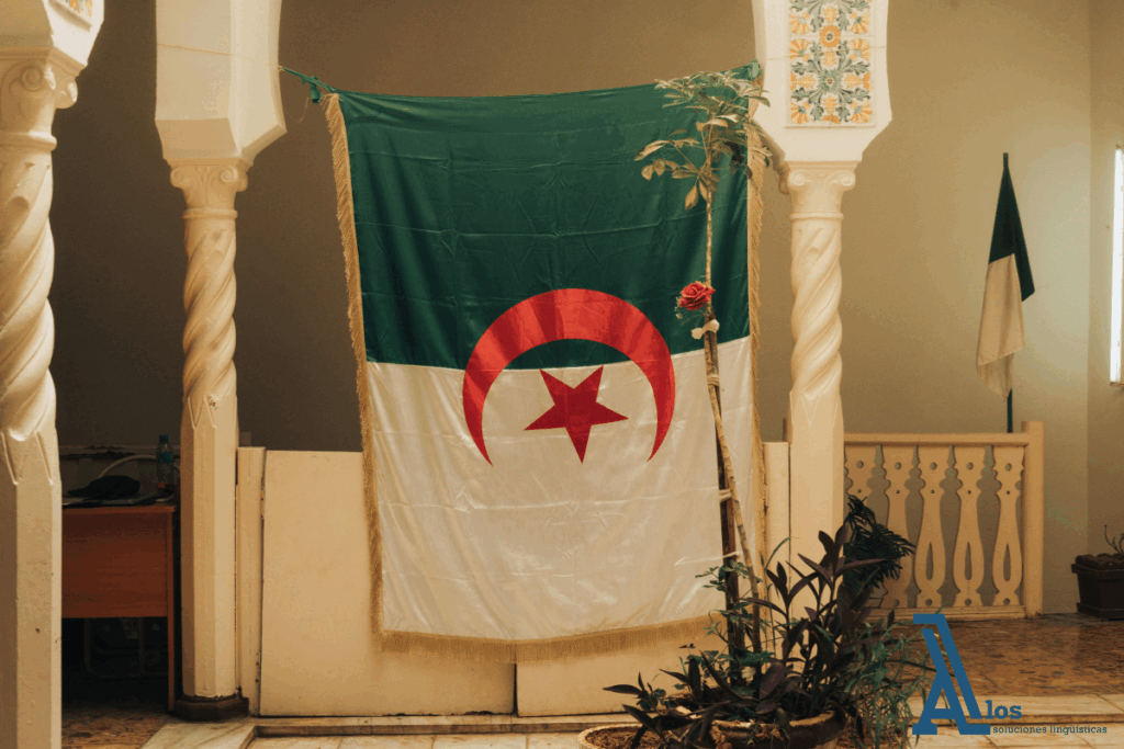 Alfombra tradicional colgada junto a la bandera de Argelia en la fachada de un edificio típico árabe.

